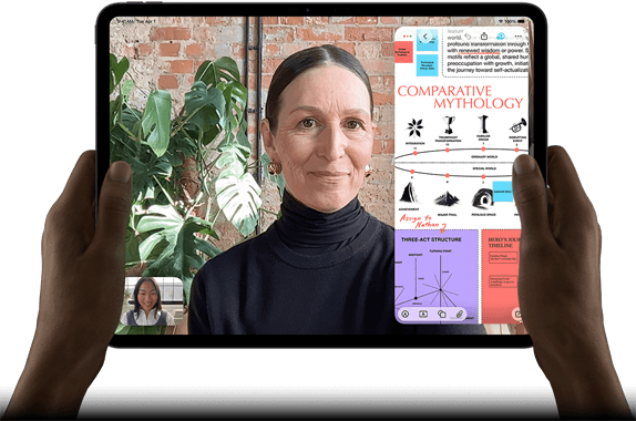 iPad Pro, Vorderansicht, Querformat, Farbe Space Schwarz, gerundete Ecken, schwarzer Displayrand, zwei Hände halten es an der linken und rechten Seite, das Display zeigt ein FaceTime Gespräch, das live übersetzt wird, und eine Lernapp zeigt eine Präsentation zum Thema „Vergleichende Mythologie“ mit Text, Diagrammen und handschriftlichen Notizen