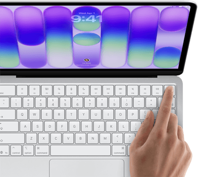 MacBook Neo, Farbe Silber, Anmeldebildschirm, ein Finger berührt den Touch ID Sensor oben rechts auf der Tastatur