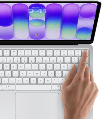 MacBook Neo, Farbe Silber, Anmeldebildschirm, ein Finger berührt den Touch ID Sensor oben rechts auf der Tastatur